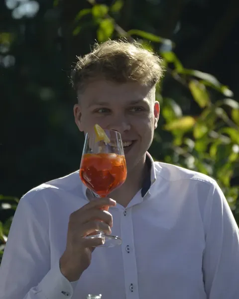 Julian hält ein Glas Aperol Spritz und lächelt